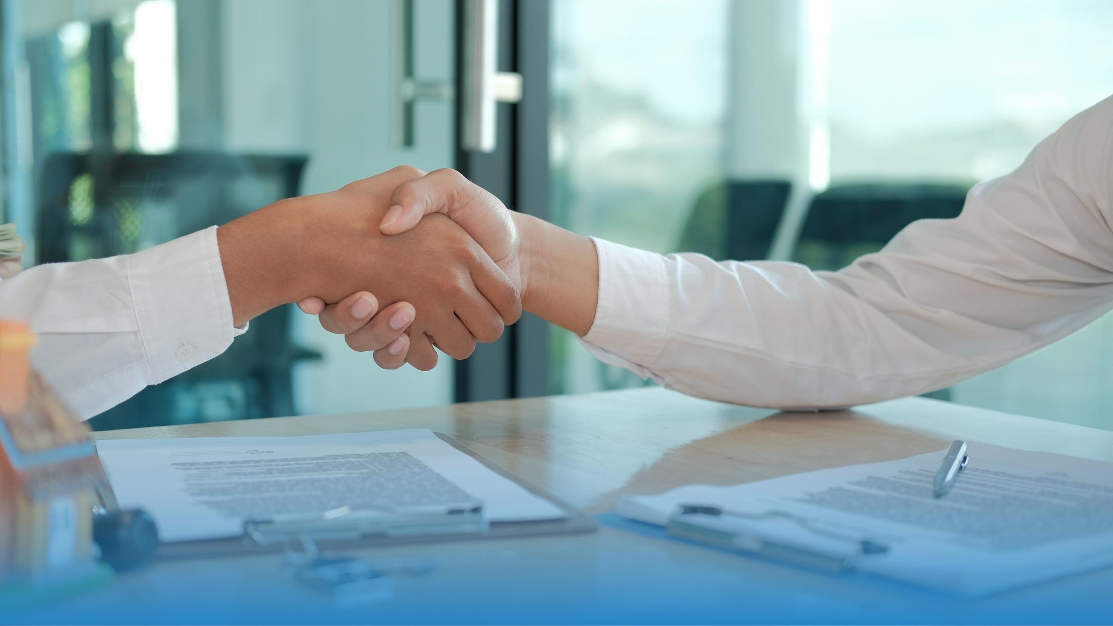 Two businessmen sit on a desk and shaking hands after streamlining their contract process by consolidating agreements