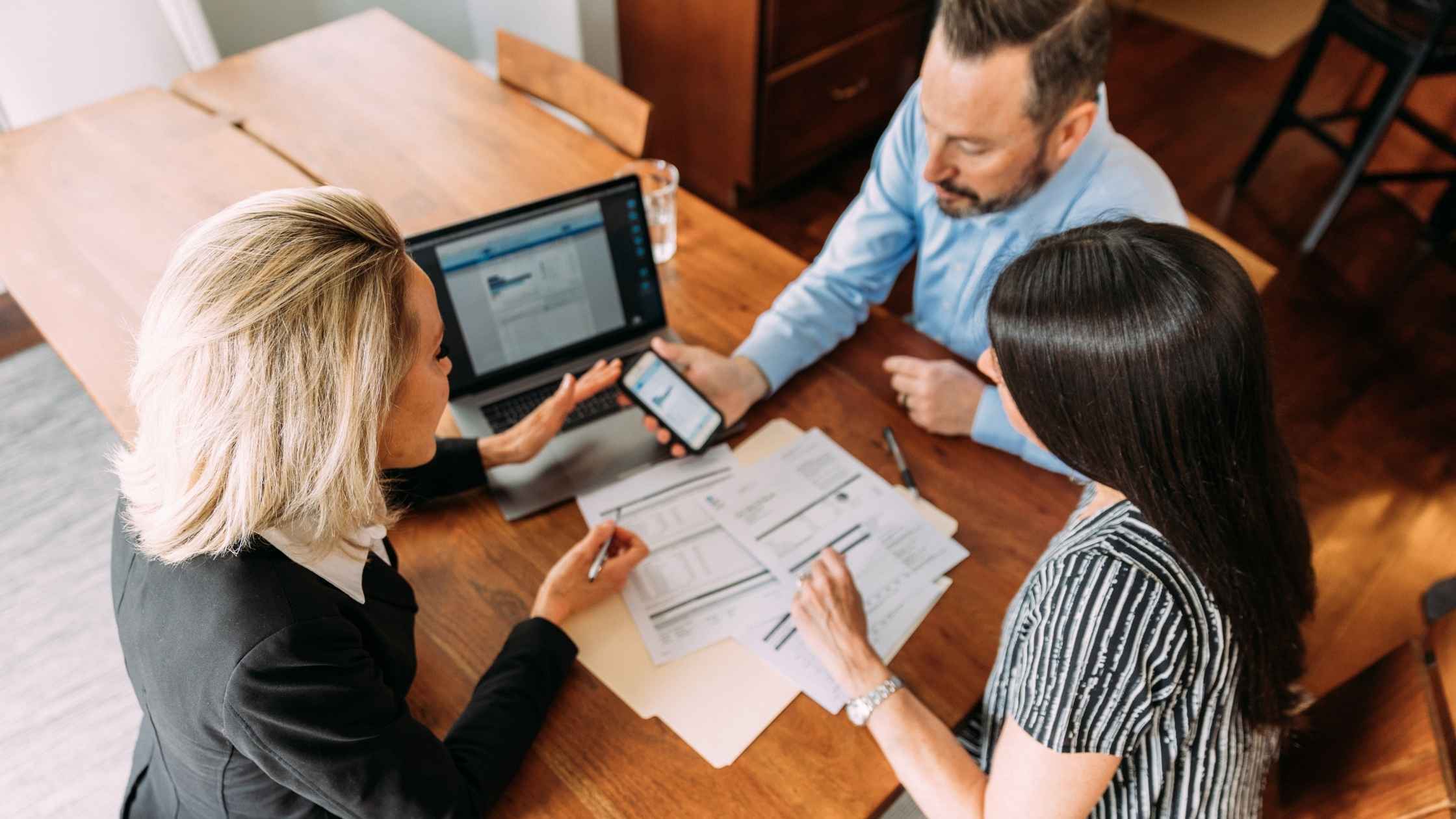 A business team reviewing financial cost of contract delays with a laptop and paper on a desk while one of them holds a cellphone