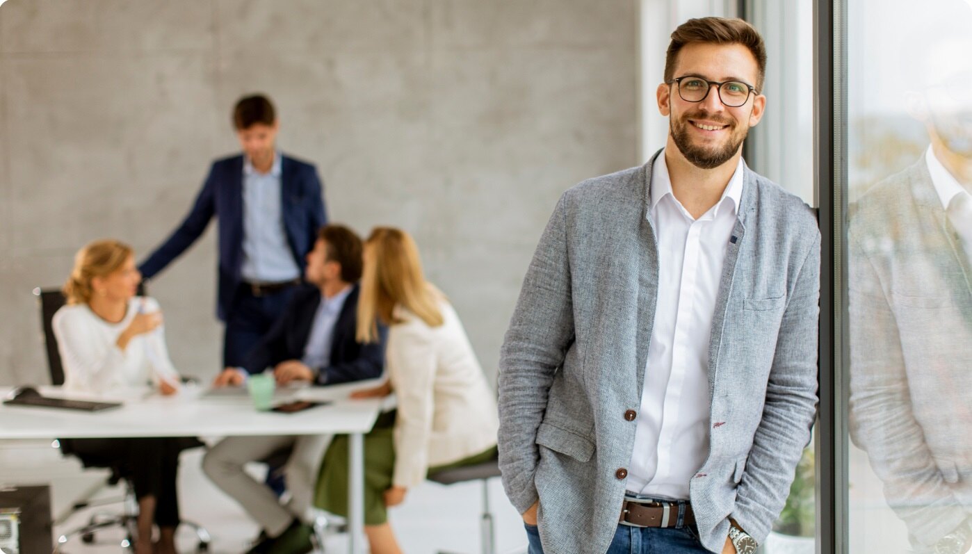 Confident professional standing by a window with a legal team collaborating in the background, symbolizing AI-enhanced contract workflows.